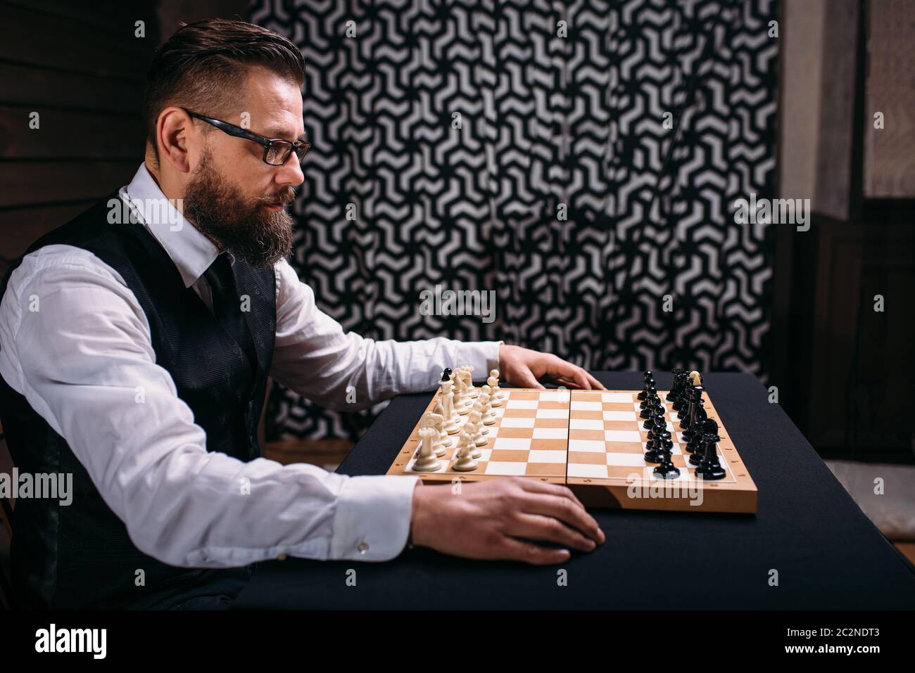 Male player in glasses sitting against the chess board with the pieces ...