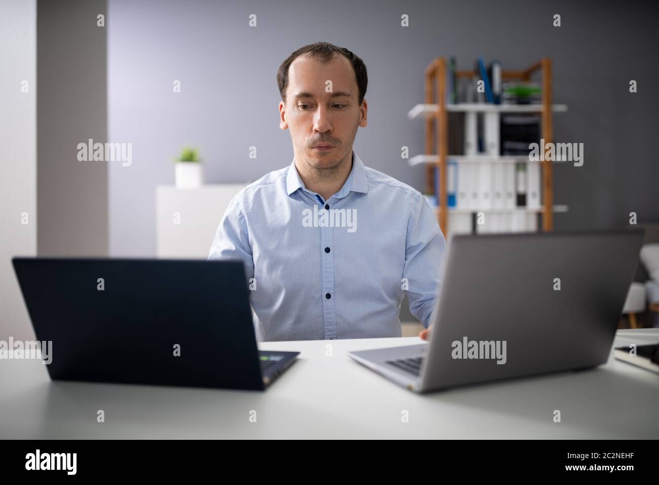 Businessperson Doing Multitasking Work On Two Laptops At Workplace Stock Photo