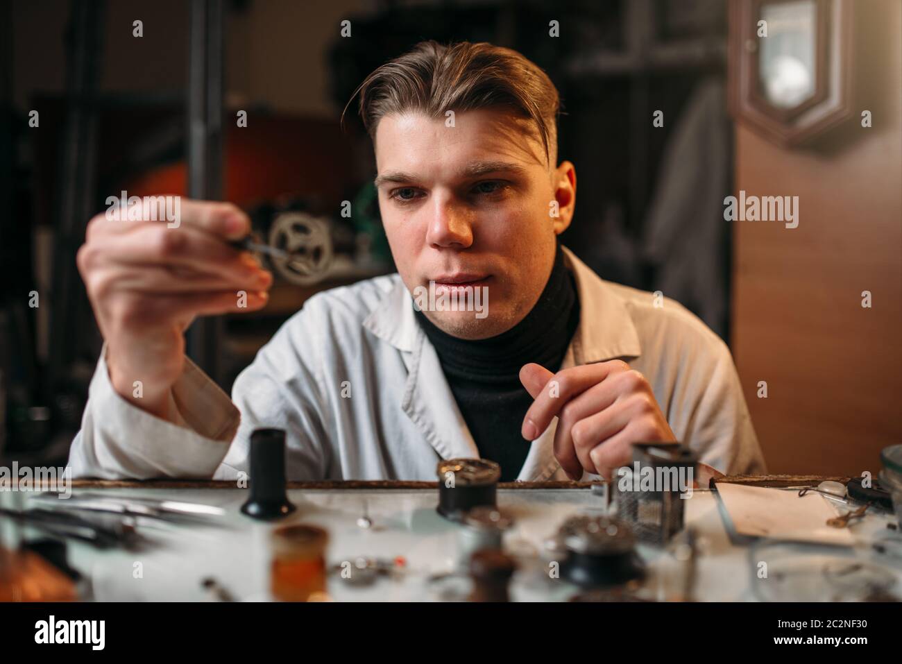 Watchmaker holding with tweezers a gear of old hours. Broken mechanical watches repairing Stock Photo