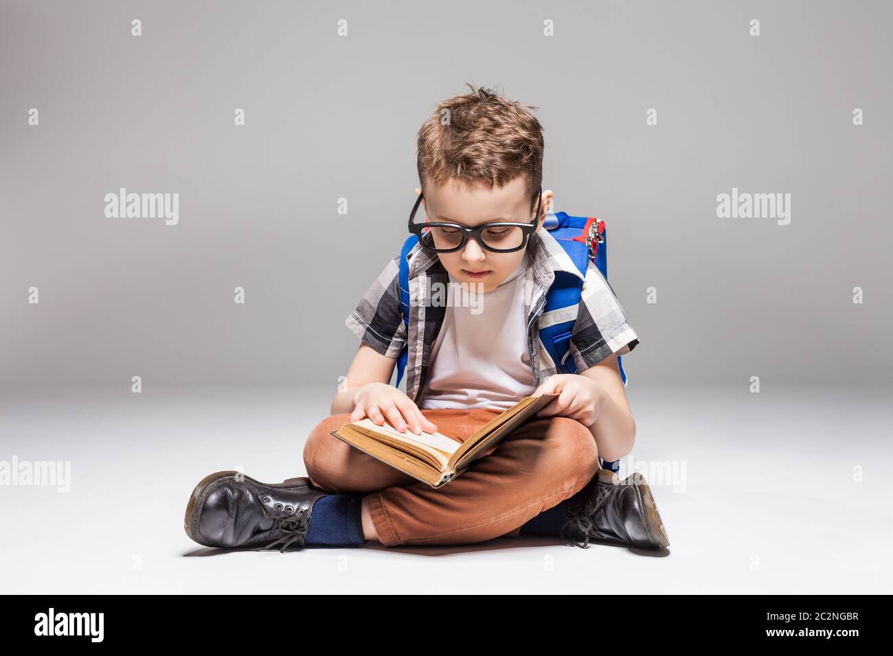 Little boy with backpack reading a book in yoga pose, studio photo ...
