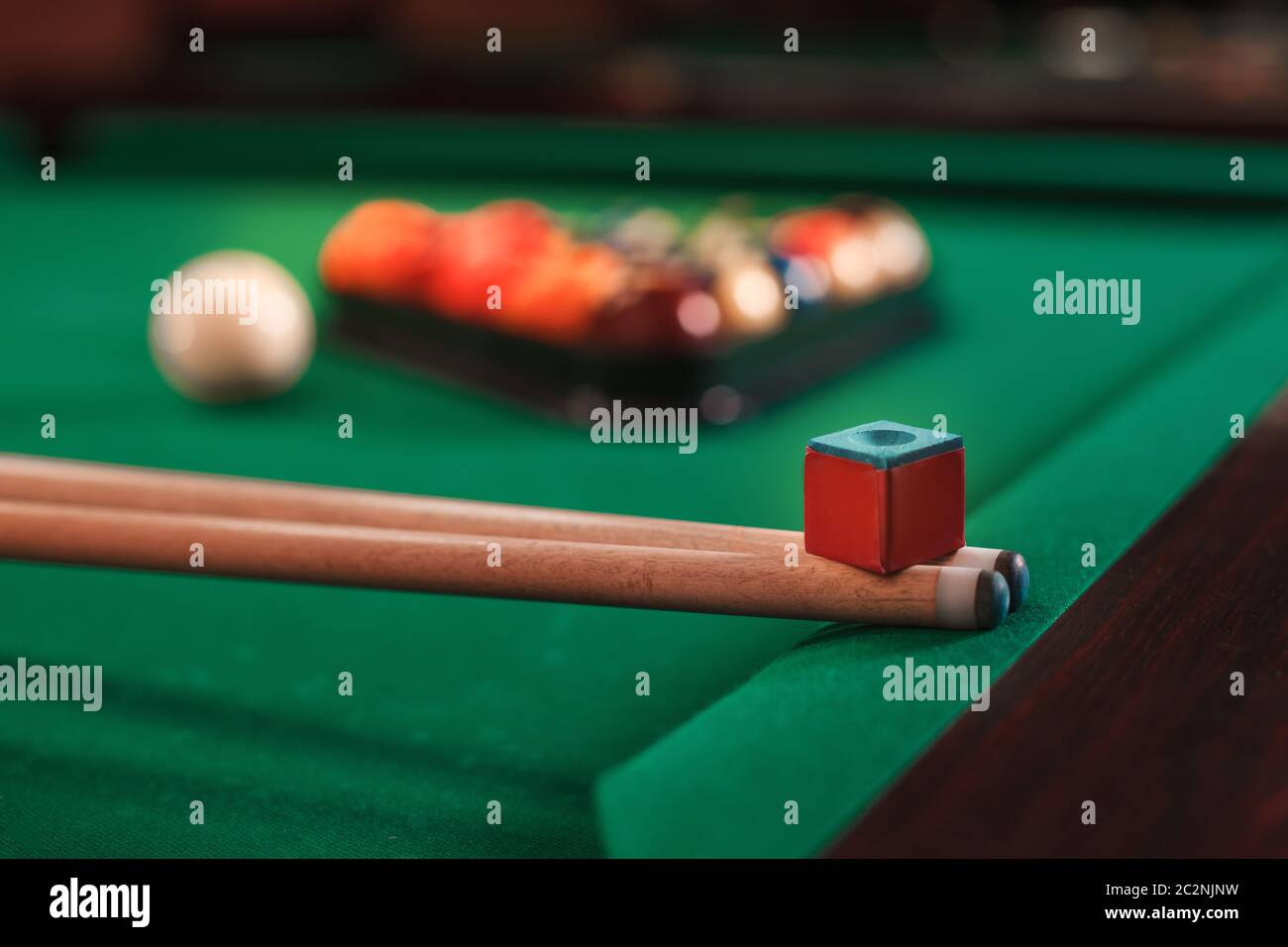 Cues and chalk on a pool table. Billiard balls in triangle on the background. Stock Photo