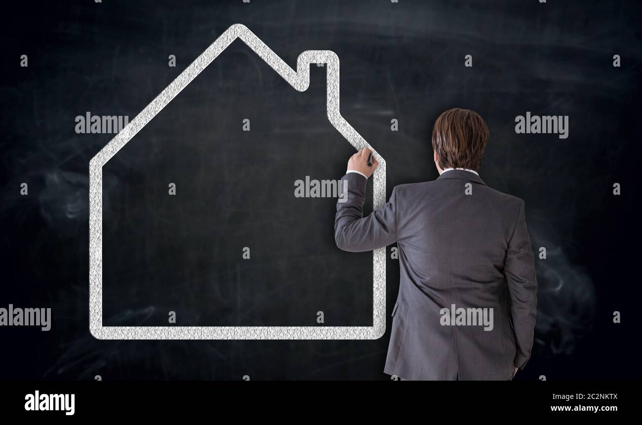 Businessman paints house on blackboard Concept. Stock Photo
