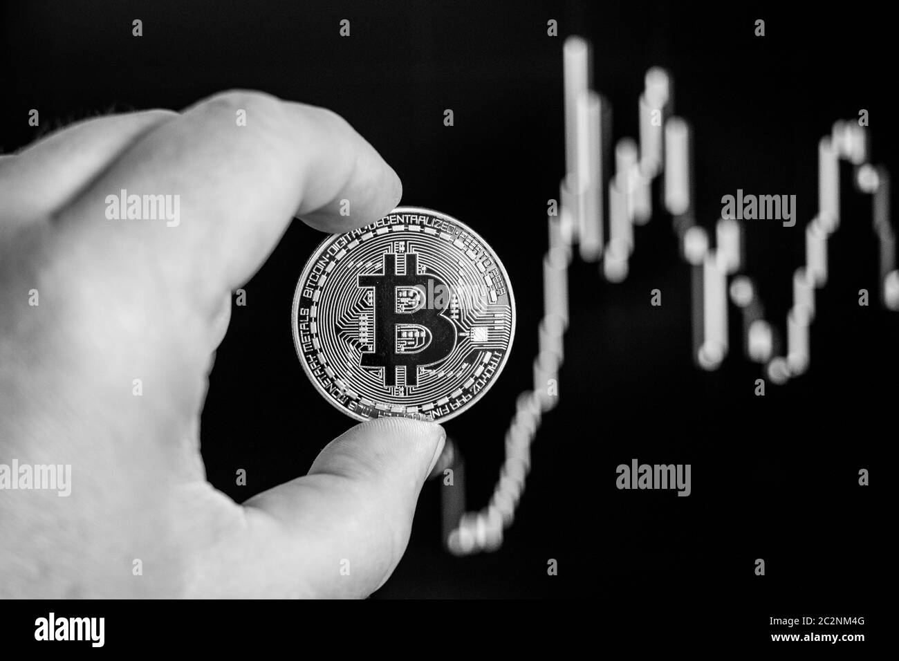 a hand holds a Bitcoin coin before a chart Stock Photo