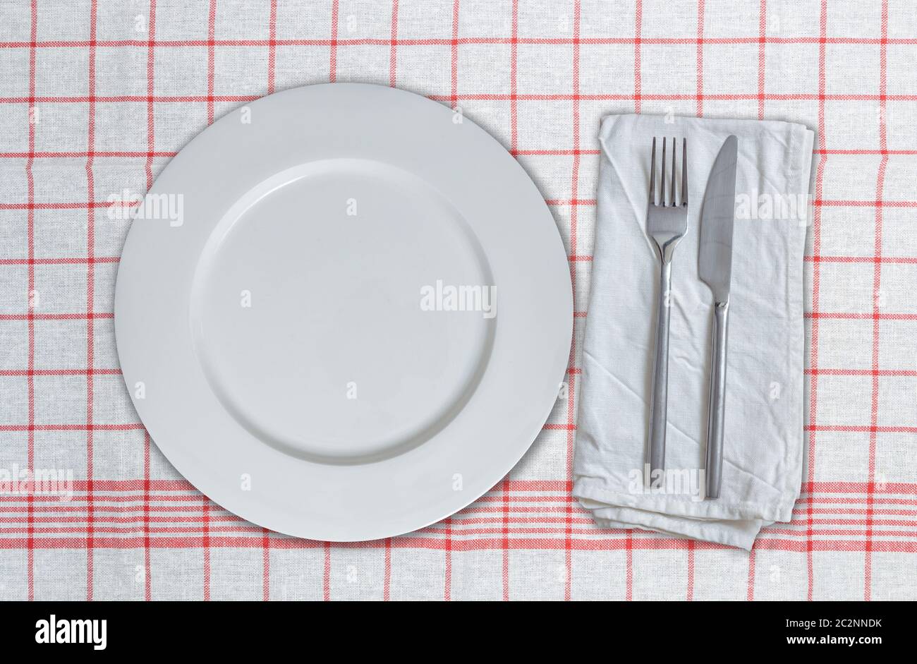 Empty dish and cutlery on red white kitchen towel. Stock Photo