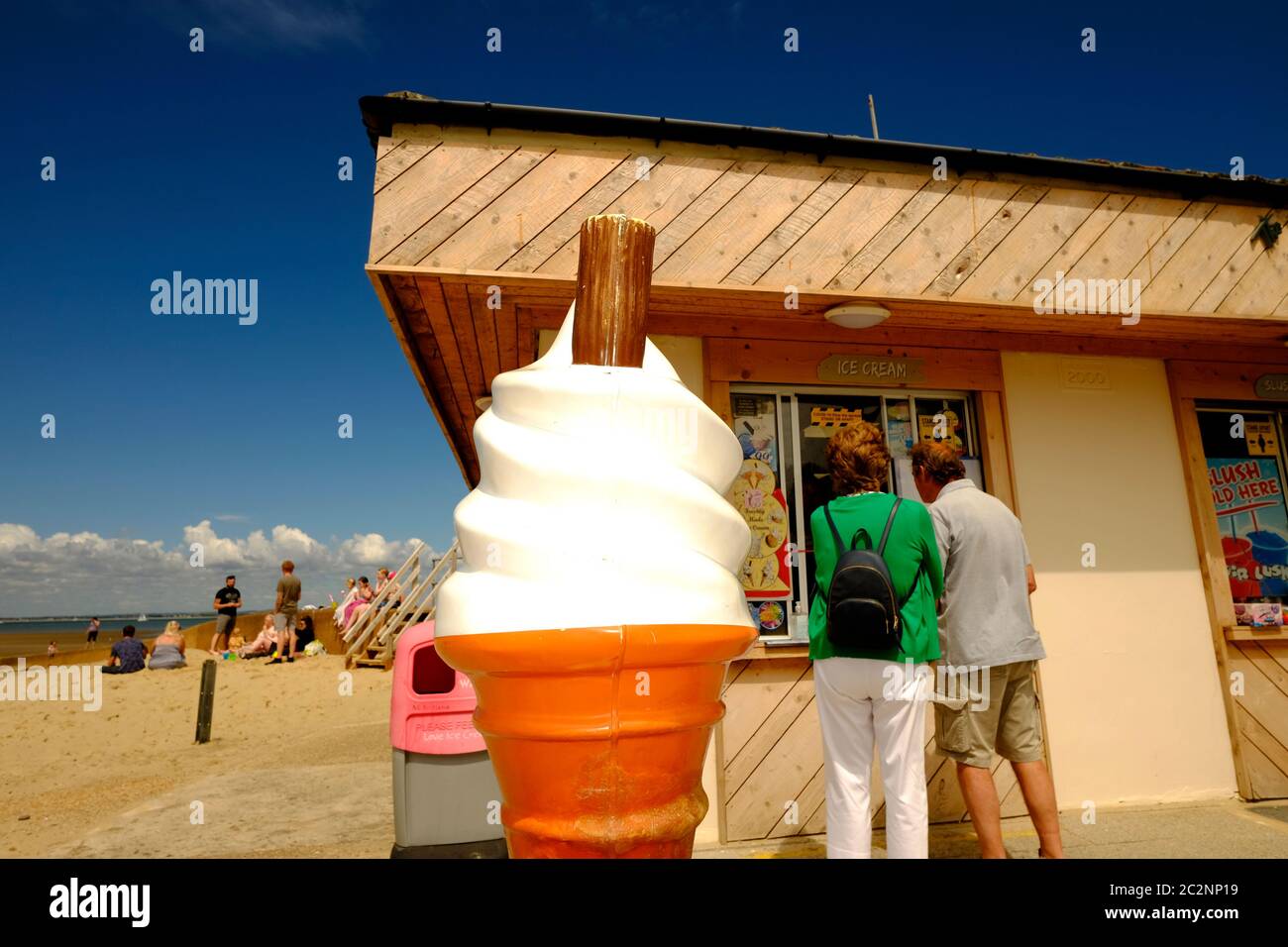 Ice cream kiosk window on sandy Ryde beach seafront on hot sunny summer day blue sky large cone advertising sign object in front customers beachgoers Stock Photo