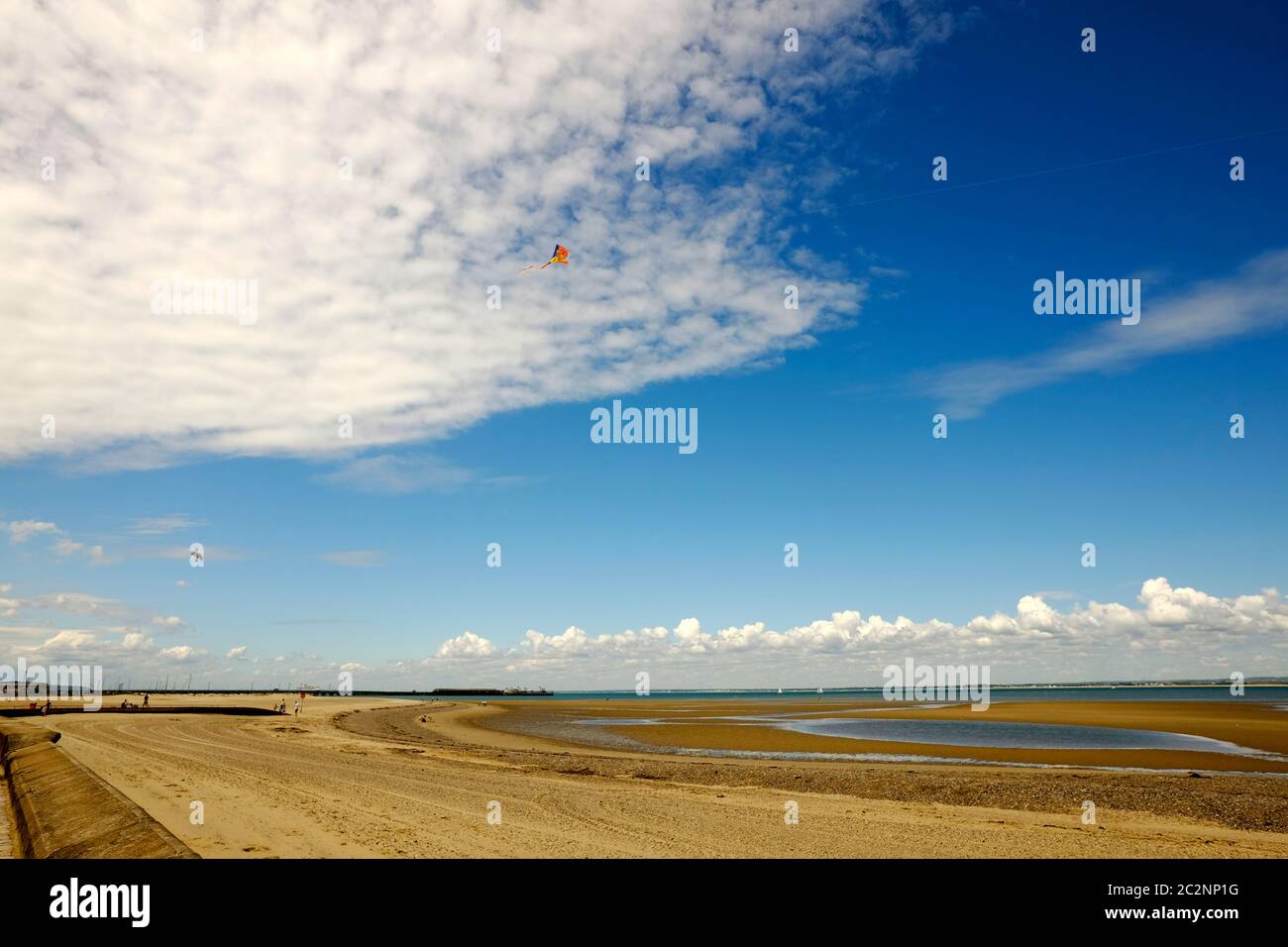 Wide expanse of sandy beach at low tide Ryde sand flats Isle of Wight colourful flying kite summer sunny day good weather blue sky high white cloud Stock Photo