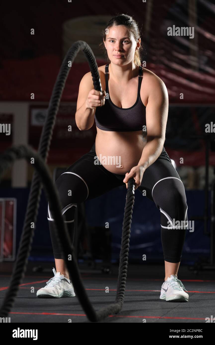 Pregnant young woman doing crossfit exercises with black ropes Stock Photo