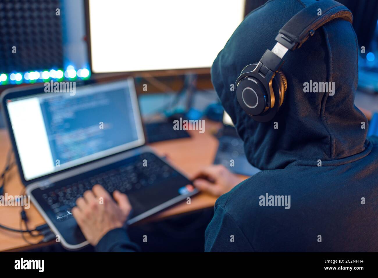 Hacker in the hood sitting at laptop, back view, information hacking ...