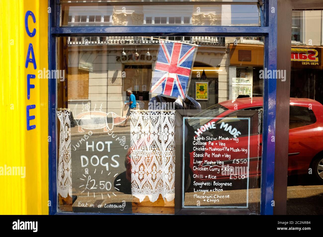 Looking at the window display of a cafe advertising prices menu boards Union Jack British flag reflections street Ventnor Isle of Wight Stock Photo