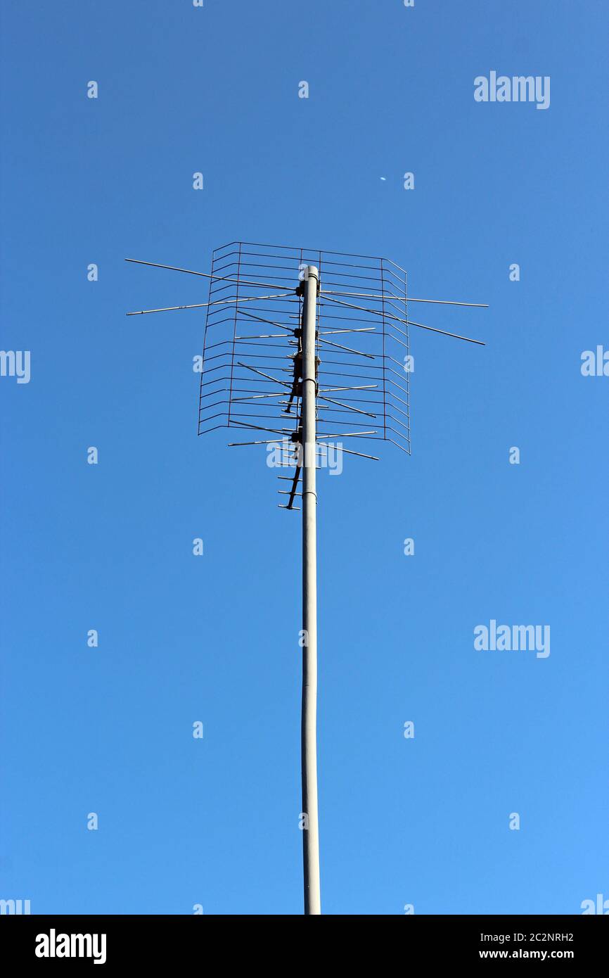 Antenna on blue sky background. Device receiving television signal. Long antenna on roof of house Stock Photo
