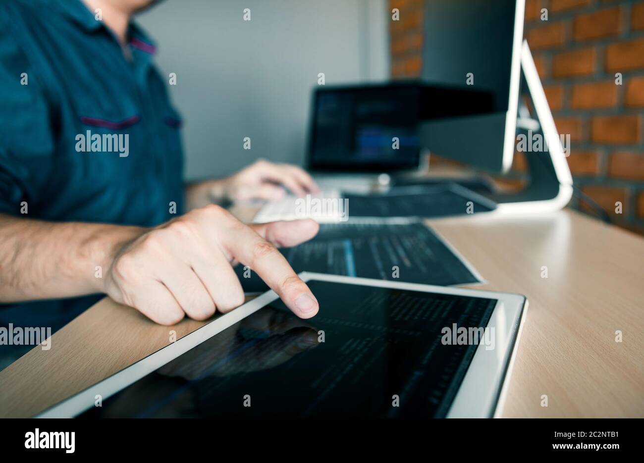 Software developer is pointing to the paper working and analyzing together the code written into the program on the computer. Stock Photo