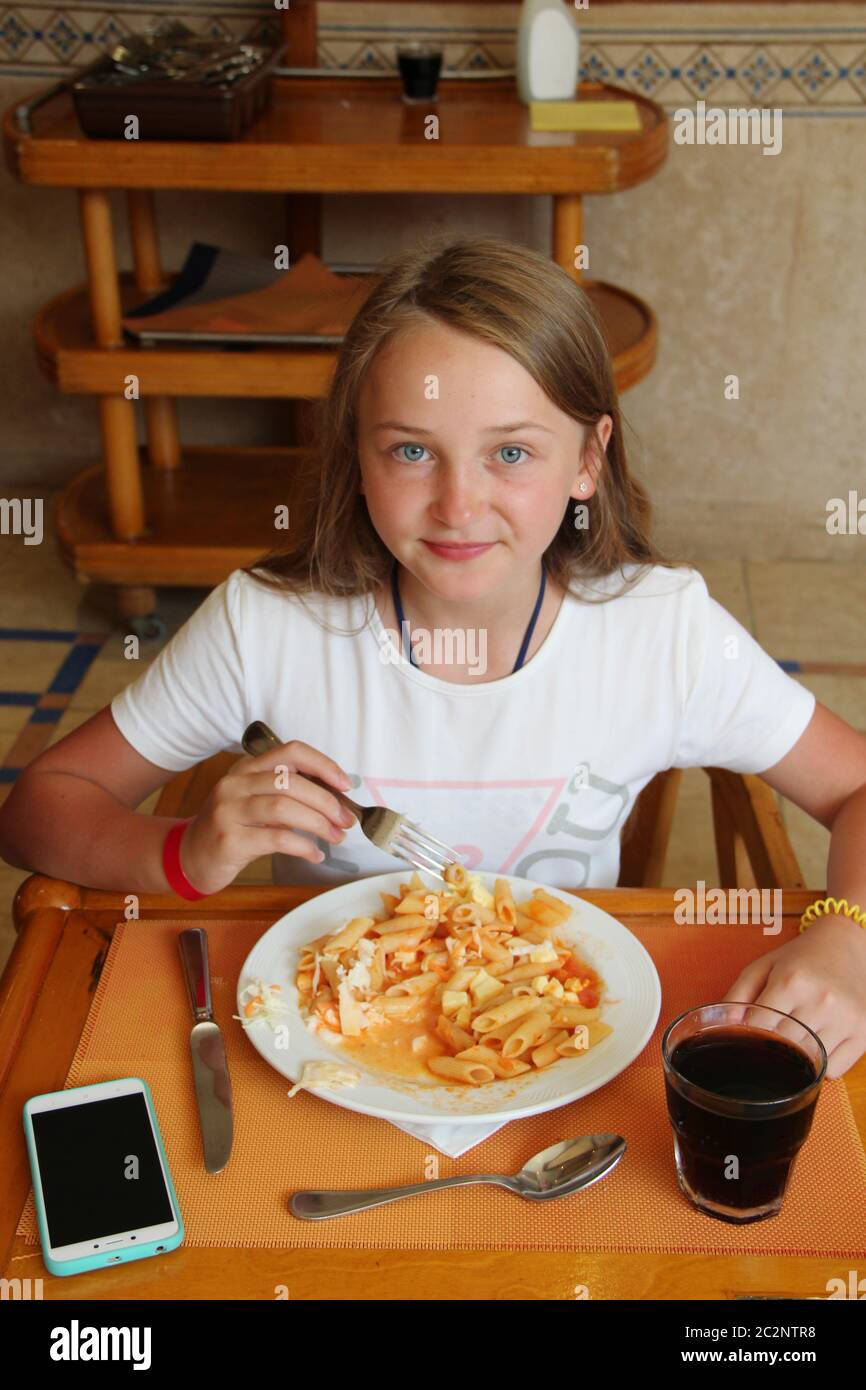 Modern child eating lunch with macaroni with sauce at restaurant. Modern little girl tourist eating Stock Photo