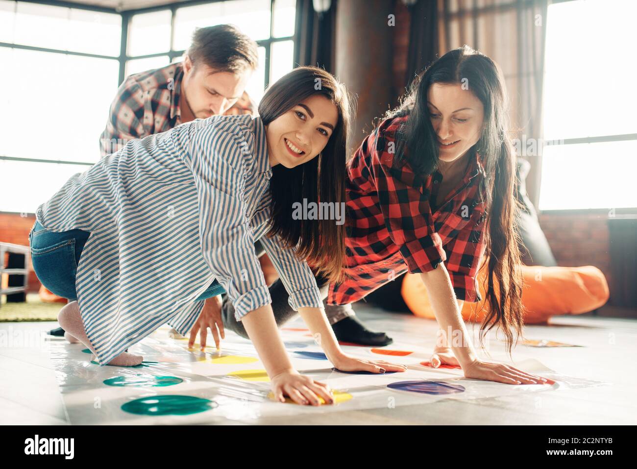 Group of students playing twister game. Youth in funny poses on the floor, entertainment for active company, friends having fun Stock Photo