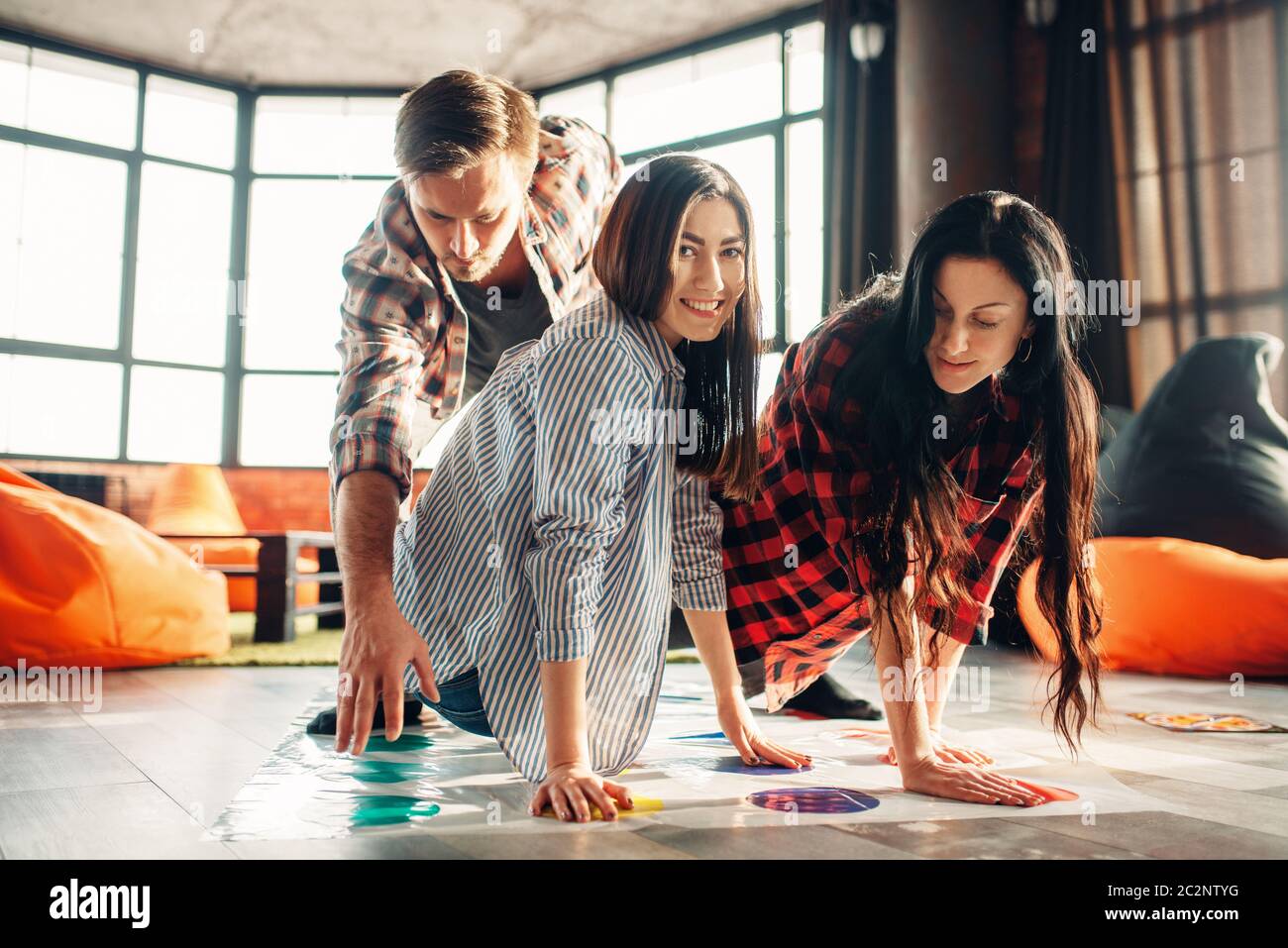 Group of students playing twister game. Youth in funny poses on the floor, entertainment for active company, friends having fun Stock Photo