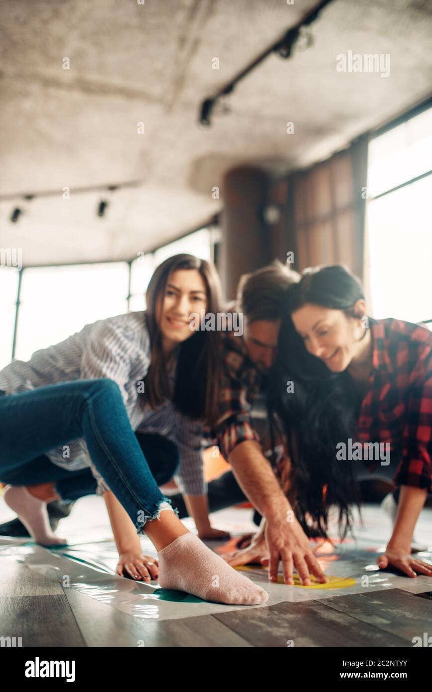Group of students playing twister game. Youth in funny poses on the floor, entertainment for active company Stock Photo