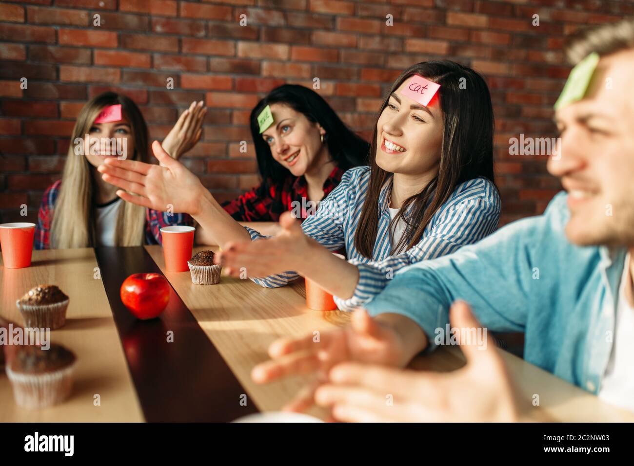 Smiling friends playing sticker notes to forehead game. Company plays who I  am at the table in cafe, guess the character Stock Photo - Alamy