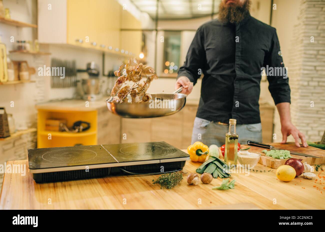 Male chef cooking meat with vetables into the frying pan on the kitchen ...