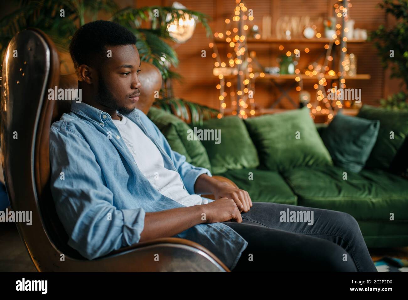 Black man sitting in a comfortable leather chair in the living room,  relaxation at home. Young african american male person in his house Stock  Photo - Alamy