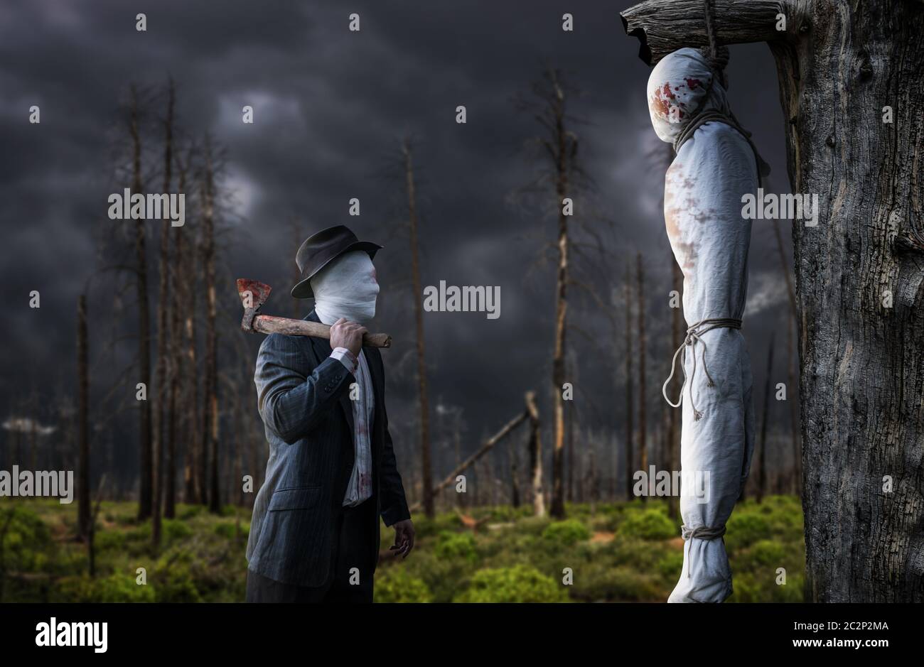 Serial maniac with an axe in front of a victim hanging on a tree, swamp and dry forest on background, bloody killer concept, psycho murderer Stock Photo