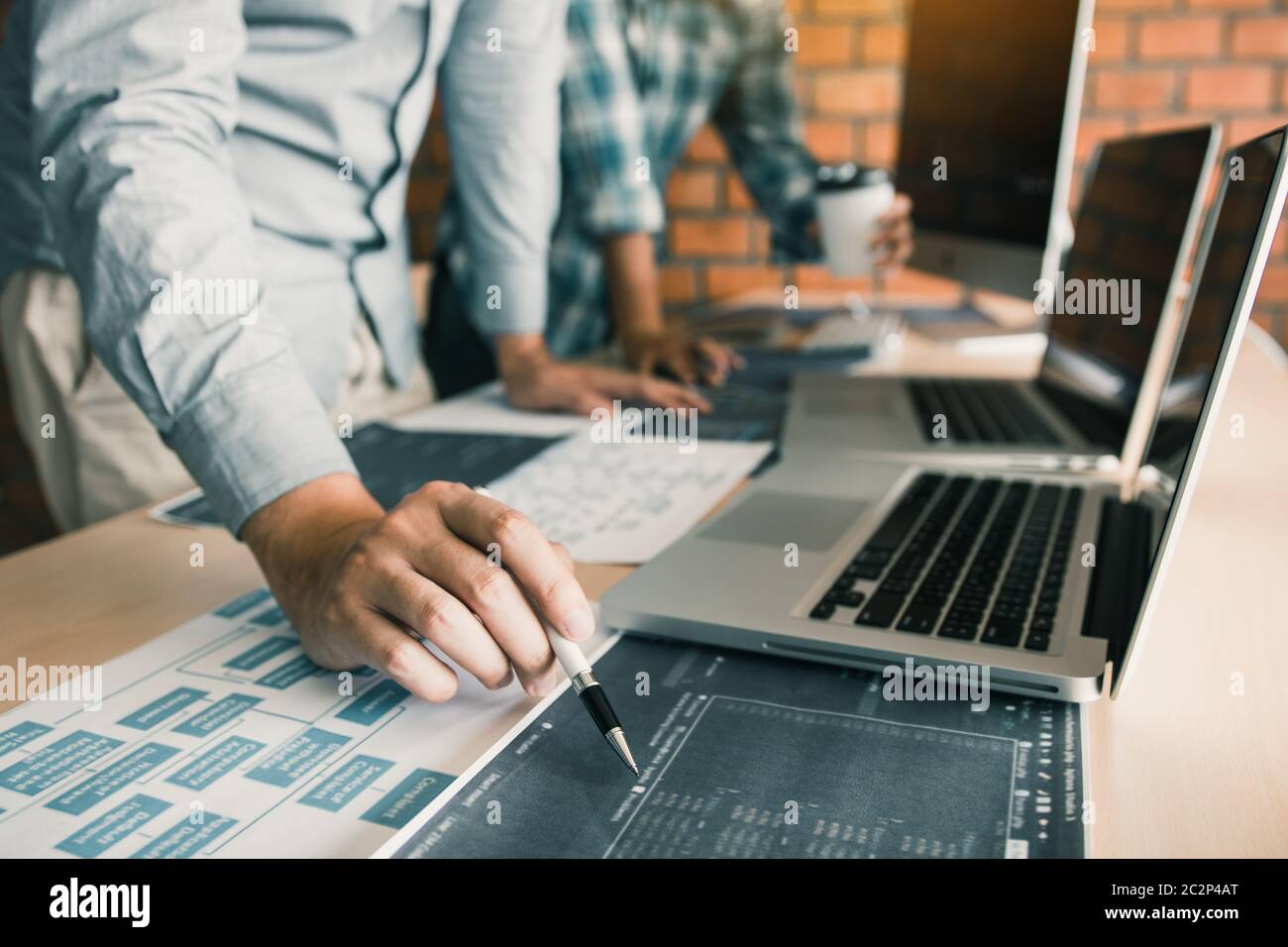 Software developer is pointing to the paper working and analyzing together the code written into the program on the computer. Stock Photo