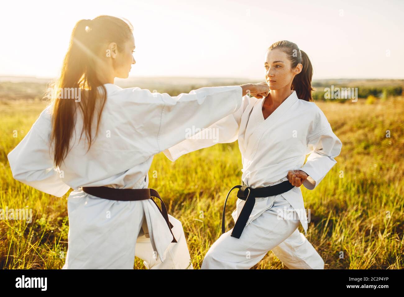 Two female karate with black belts fight in summer field. Martial art