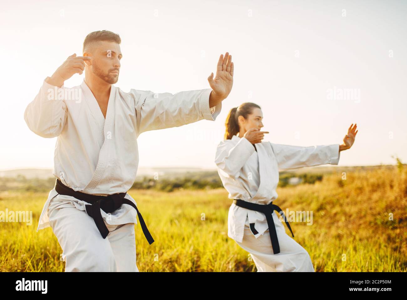 Male and female karate masters with black belts fight in summer field