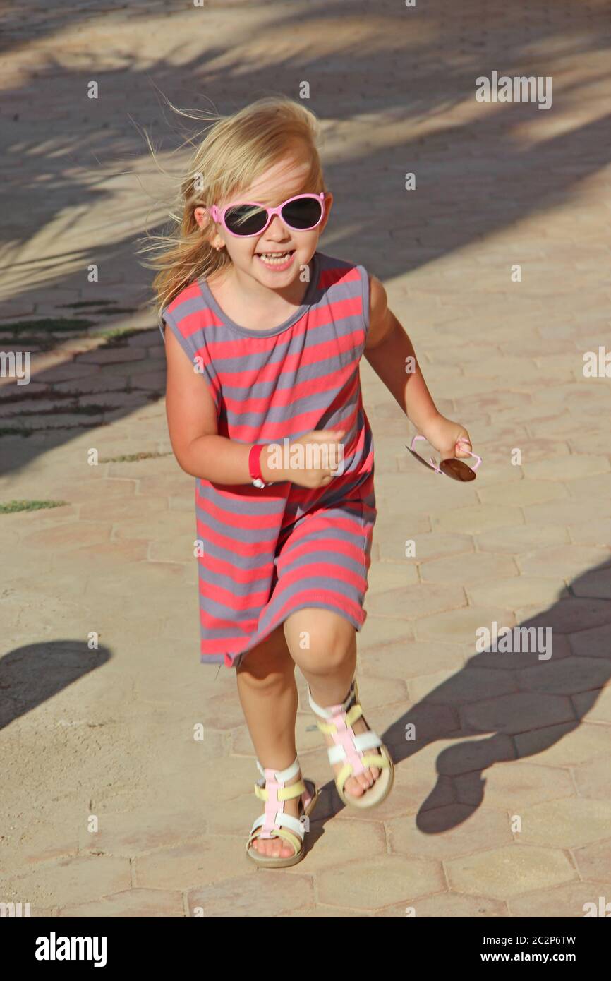 Happy little girl running in city park. Positive childish emotions. Child running along path smiling Stock Photo
