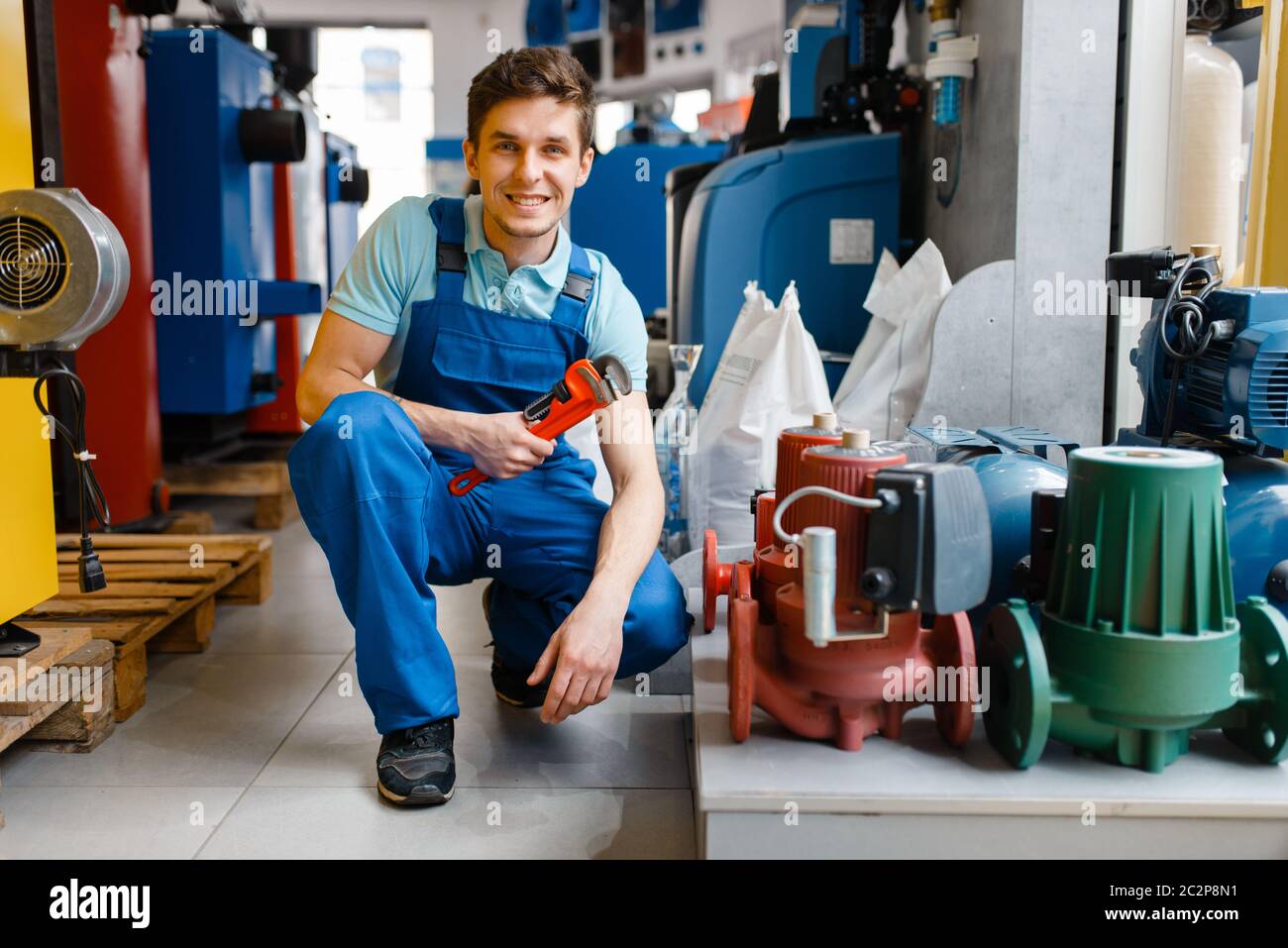 Plumber with pipe wrench at the showcase in plumbering store. Man buying sanitary engineering in shop, pumps and water heaters choice Stock Photo