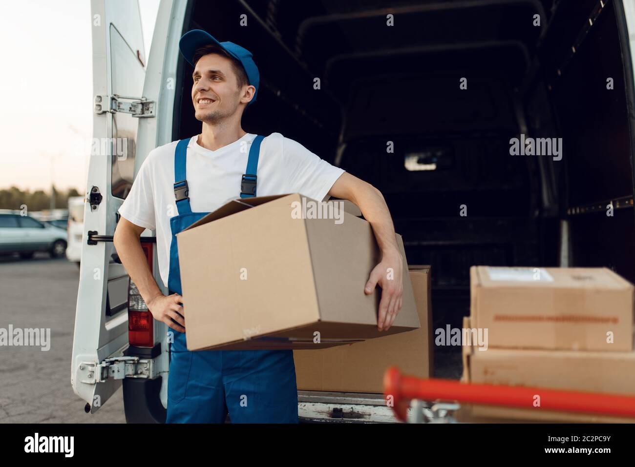 Loader in uniform holding carton box, delivery service. Man standing at