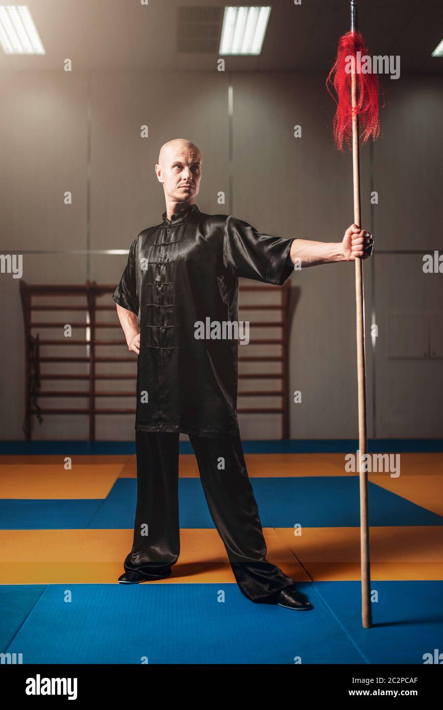 Wushu fighter poses with lance, martial arts. Man in black cloth poses with blade Stock Photo