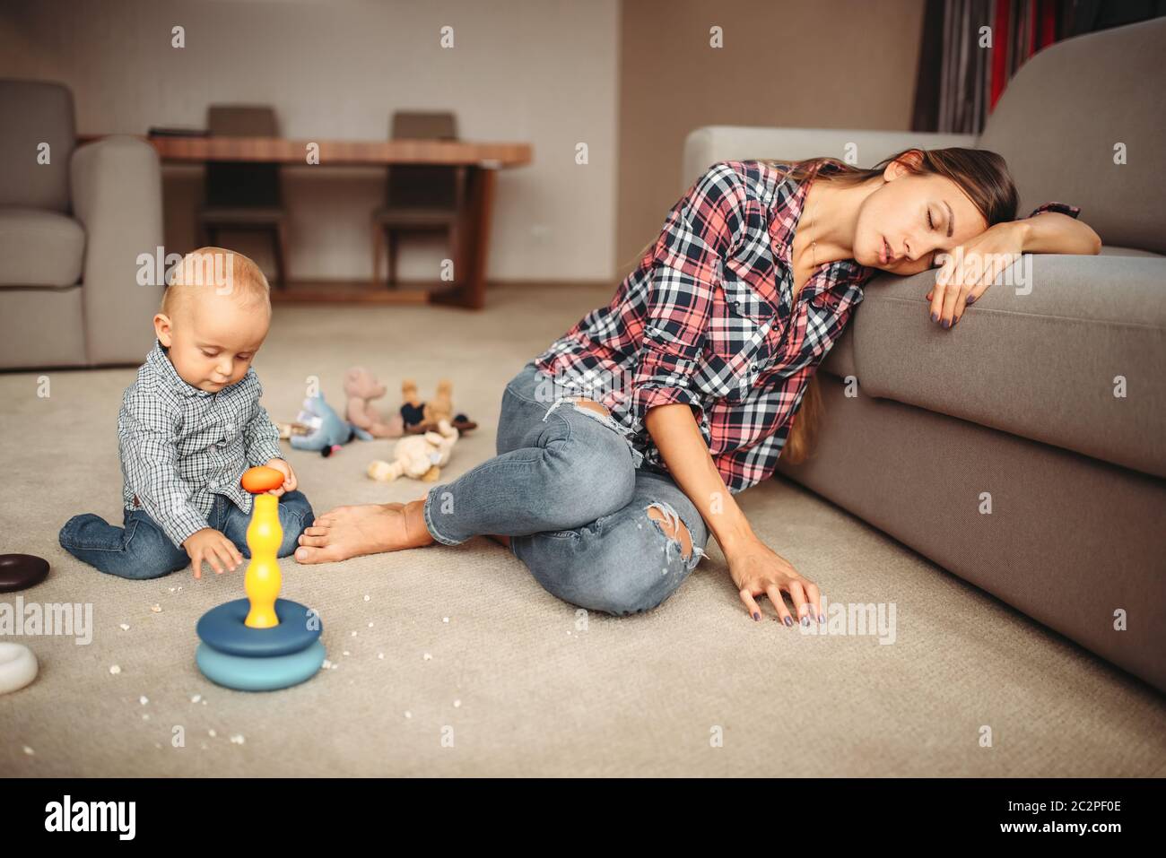 Little kid playing on the floor, mother sleeps, motherhood problems