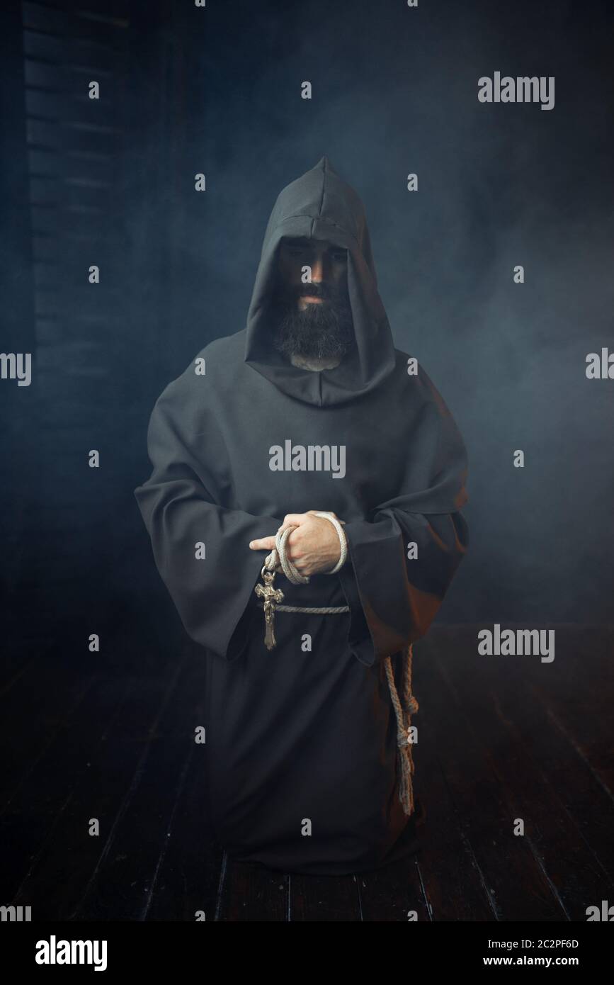 Medieval monk holds wooden cross in hands and praying, religion. Mysterious  friar in dark cape. Mystery and spirituality Stock Photo - Alamy