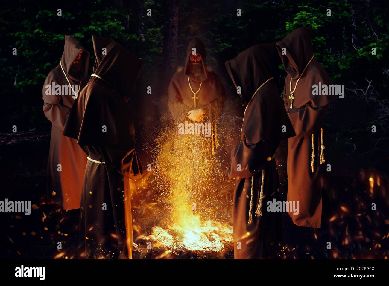 Medieval monks praying against a big fire in the night, secret ritual. Mysterious friar in dark cape. Mystery and spirituality Stock Photo