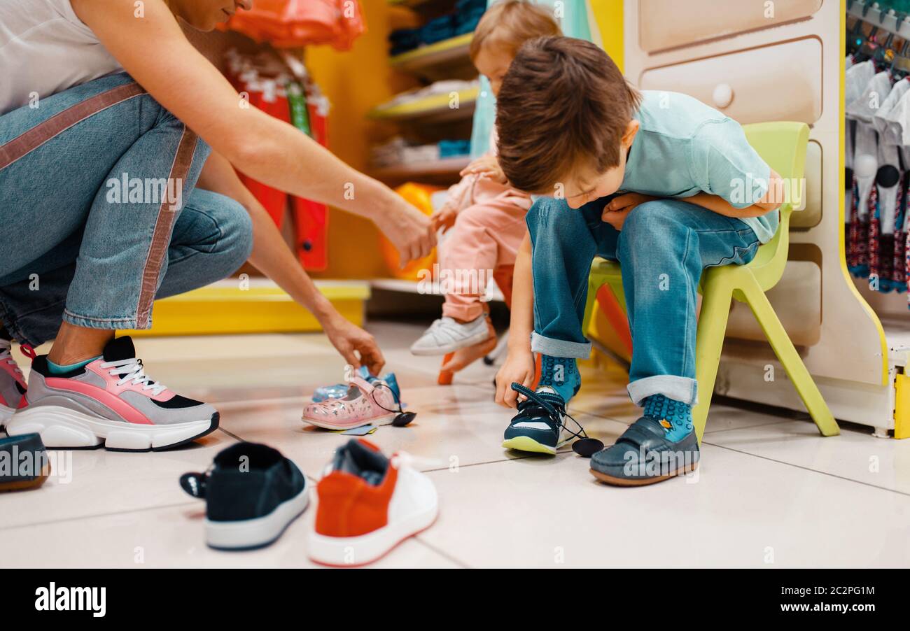 Mother with her little children choosing shoes in kids store. Happy mom