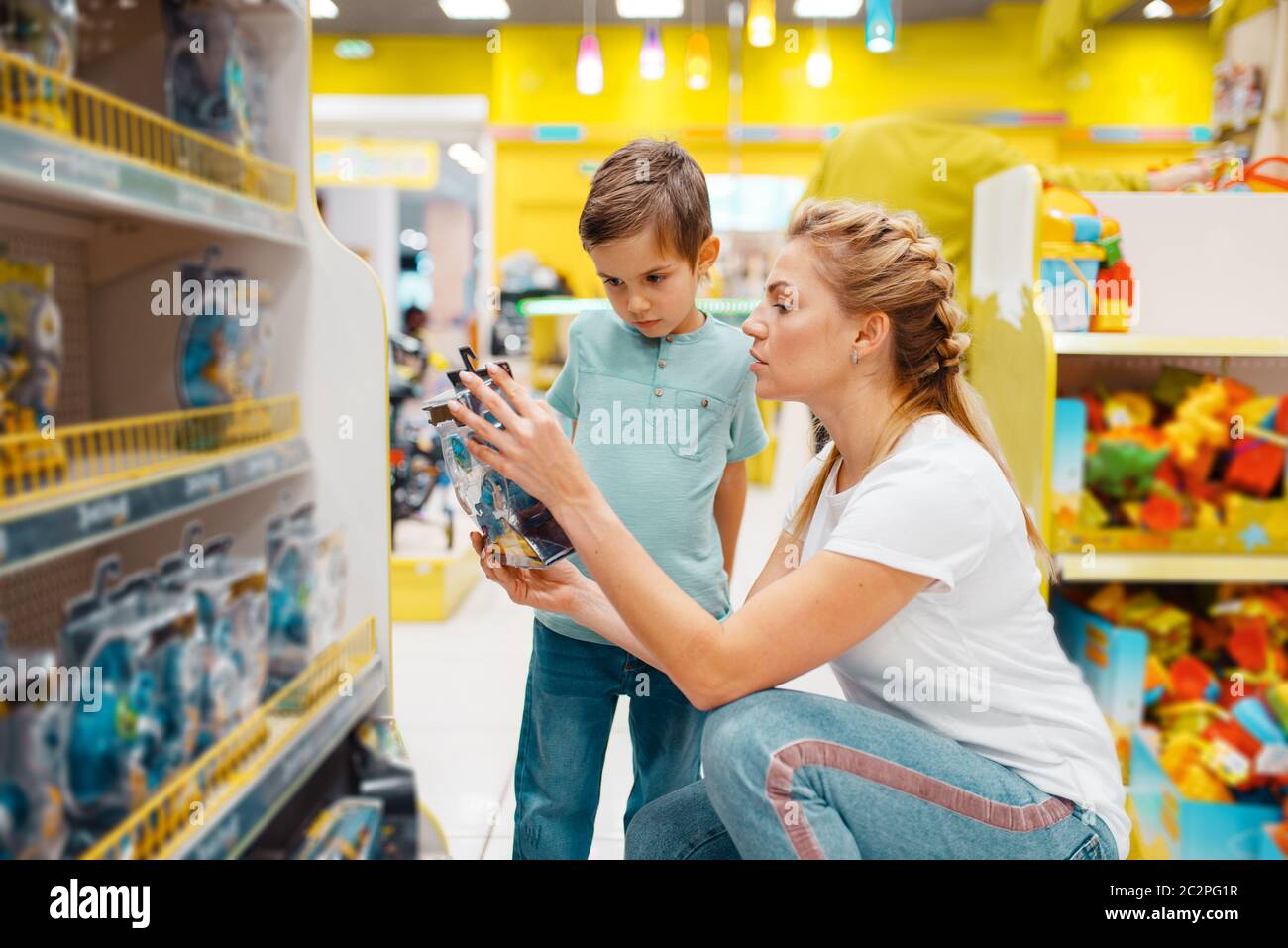 Happy mother with her little son choosing toys in kids store. Mom