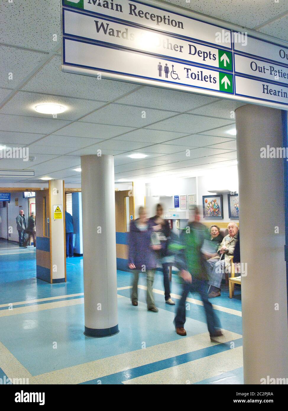 Busy UK NHS hospital and healthcare outpatients departments at a British Hospital. Patients sitting, walking and moving and doctor going through doors Stock Photo