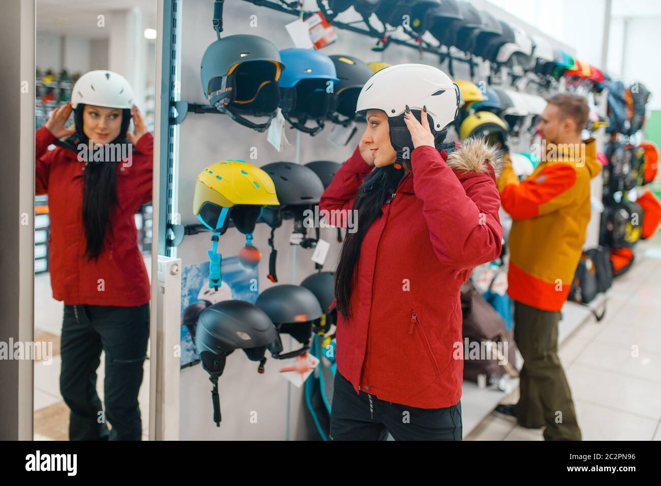 Young woman trying on helmet for ski or snowboarding at the mirror, side view, sports shop. Winter season extreme lifestyle, active leisure store, buy Stock Photo