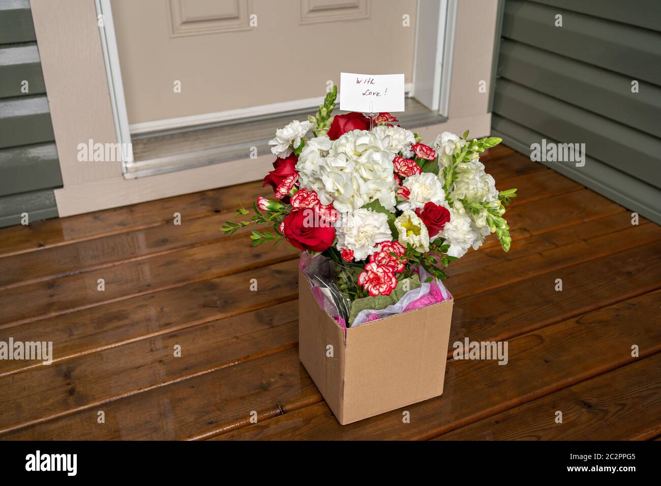A bouquet of red white flowers in a carton box on a porch doorstep of a