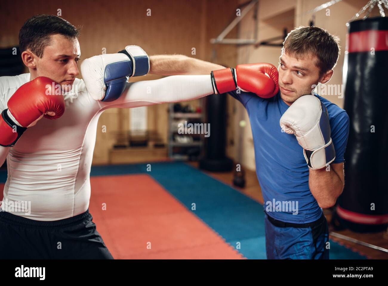Two male kickboxers in gloves practicing on workout in the gym