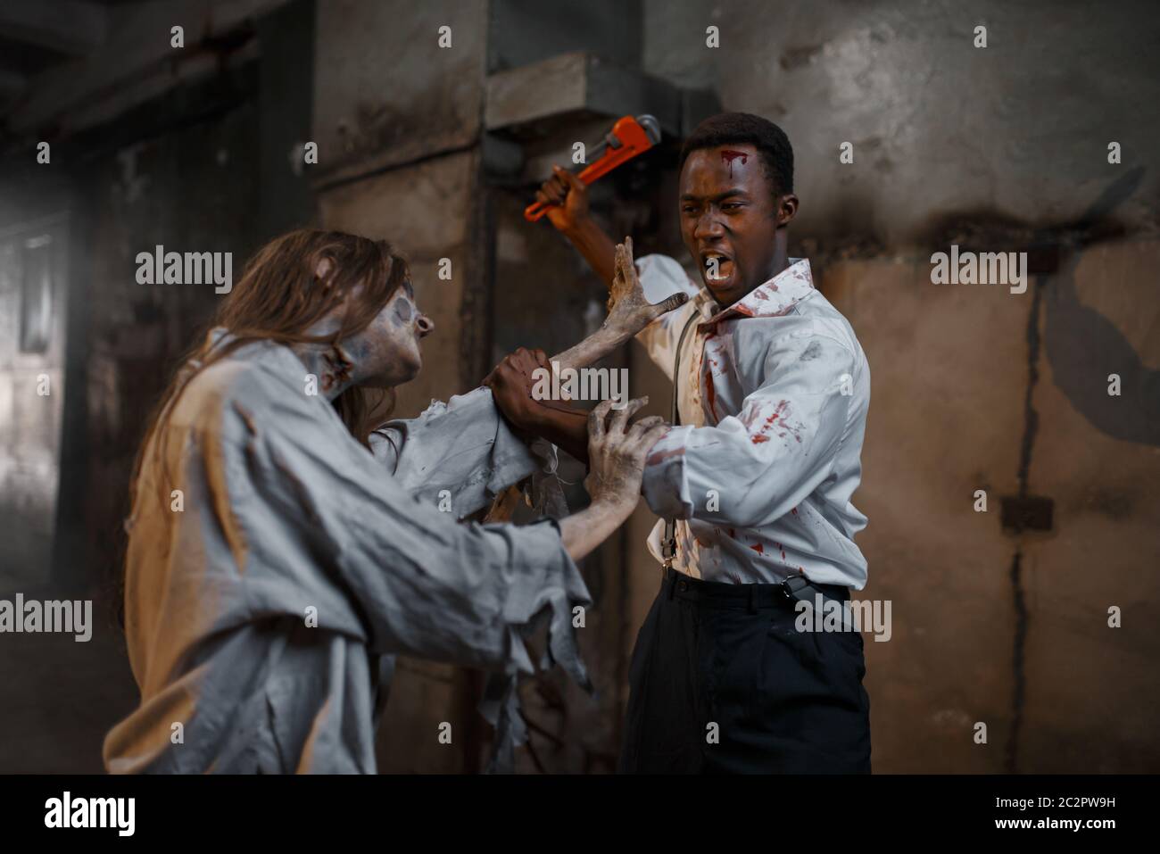 Man with pipe wrench kills female zombie, deadly chase. Horror in city, creepy crawlies attack, doomsday apocalypse, spooky bloody monster Stock Photo