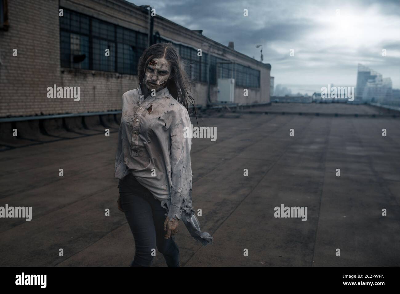 Scary female zombie on the roof of abandoned building, deadly chase. Horror in city, creepy crawlies attack, apocalypse Stock Photo