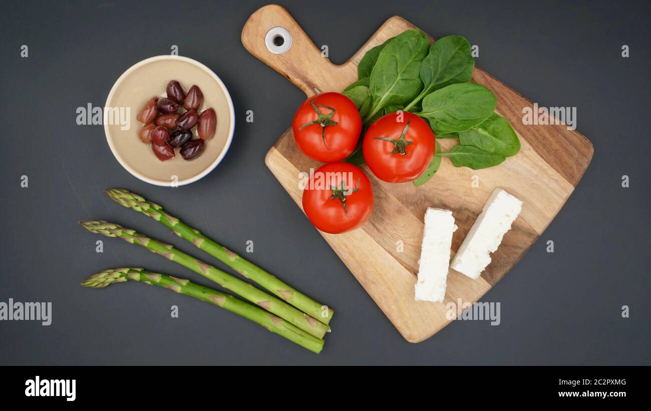 A selection of fresh produce to make a Greek salad with feta cheese, tomatoes, spinach, asparagus and Kalamata olives Stock Photo