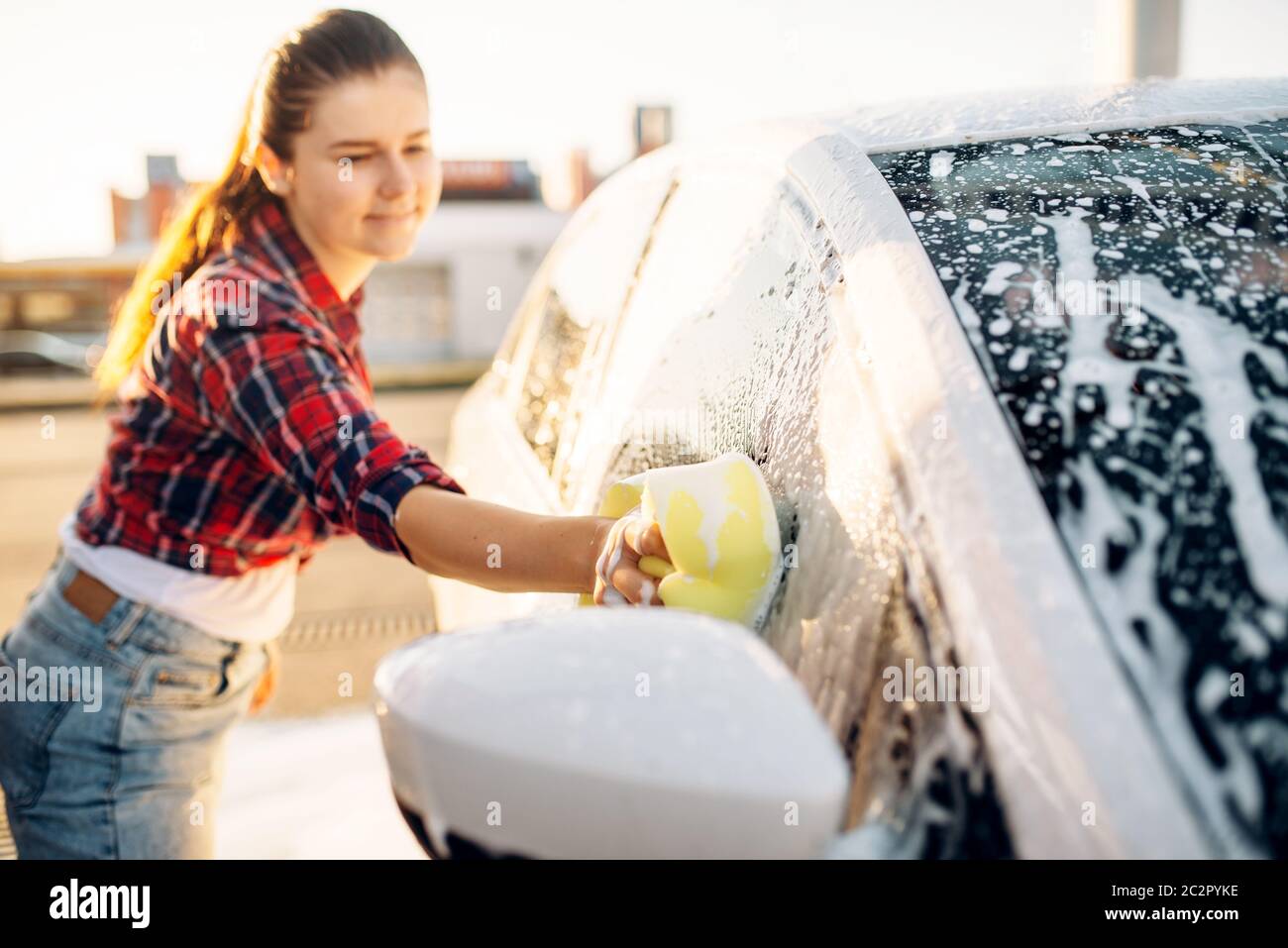 Female person hand with sponge scrubbing vehicle with foam, car