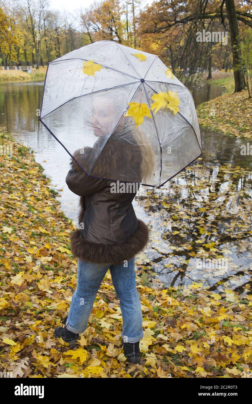 woman under a transparent umbrella on autumn day on the river shore ...
