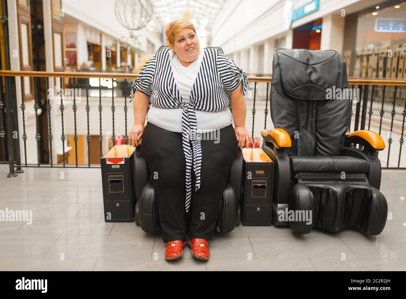 Fat woman is not placed in a massage chair in mall. Overweight female person tries to sit in a