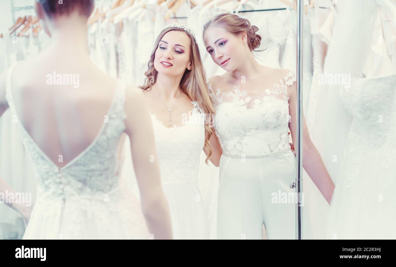 Two brides of same sex wedding couple looking at dress mannequin choosing what to wear Stock Photo