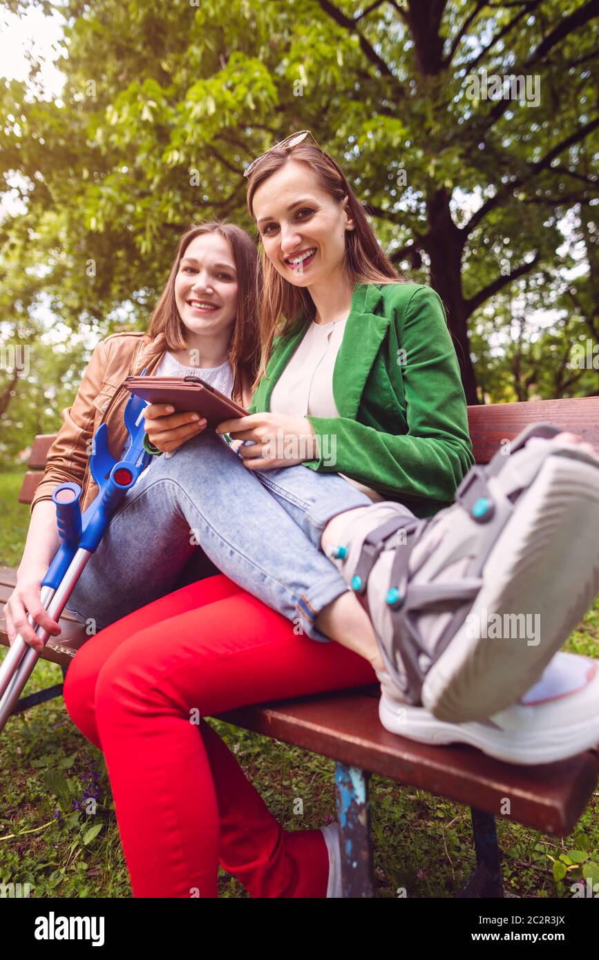 Two best friends, one with an injured leg, reading a book together Stock Photo