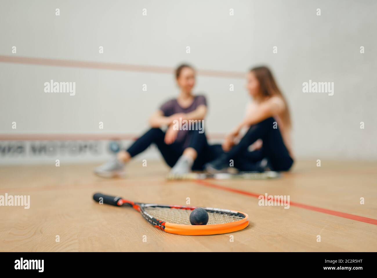 Two female players with squash rackets sits on court floor. Girls on ...