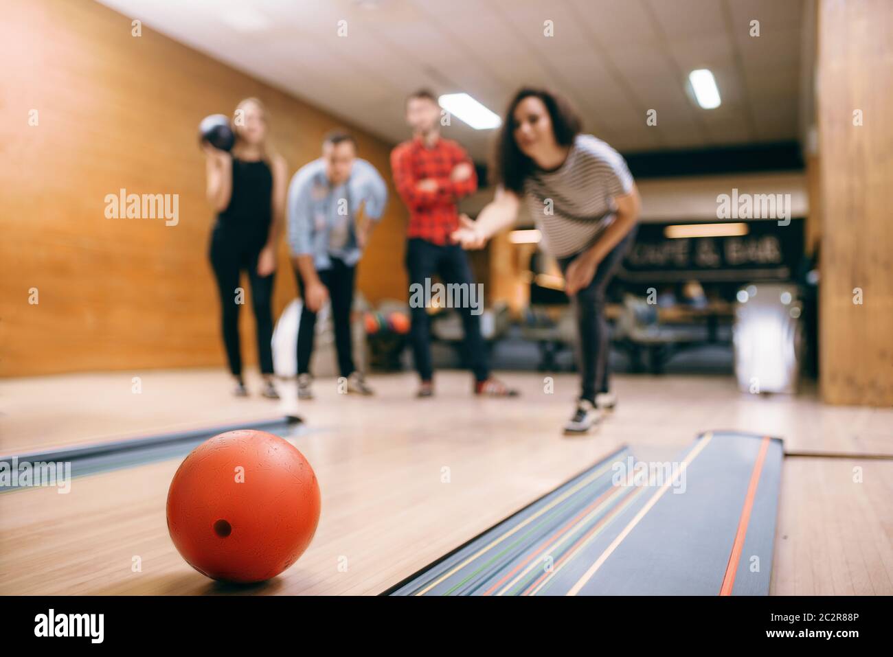 Female bowler throws ball on lane, strike shot. Bowling alley teams playing the game in club, active leisure Stock Photo