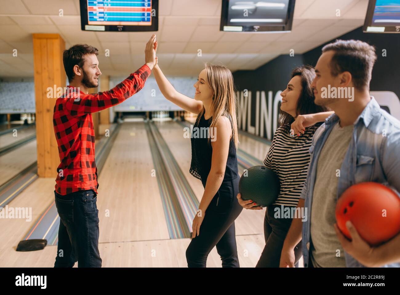 Bowler throws ball on lane and makes strike shot. Bowling alley team congratulates each other, successful throwing. Men and women playing the game in Stock Photo